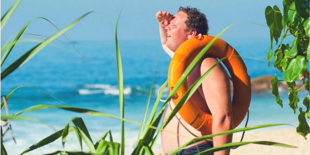 gruby mężczyzna stoi na plaży z kołem ratunkowym przerzuconym przez ramię - body positive