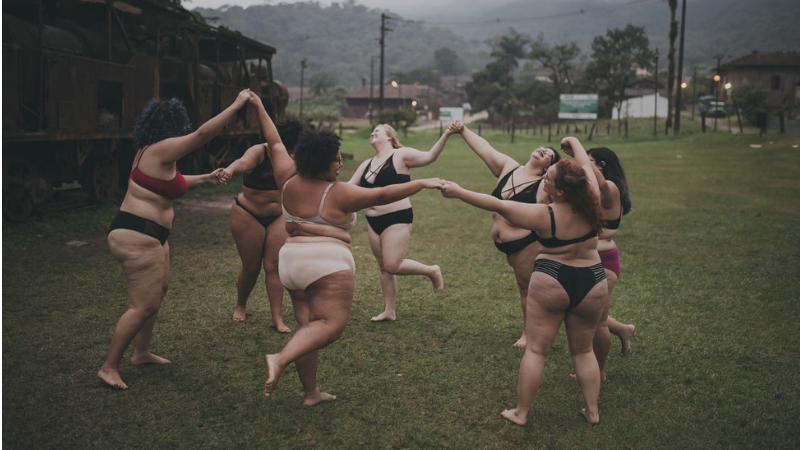 grupa grubych kobiet tańczy w samej bieliźnie, trzymając się za ręce