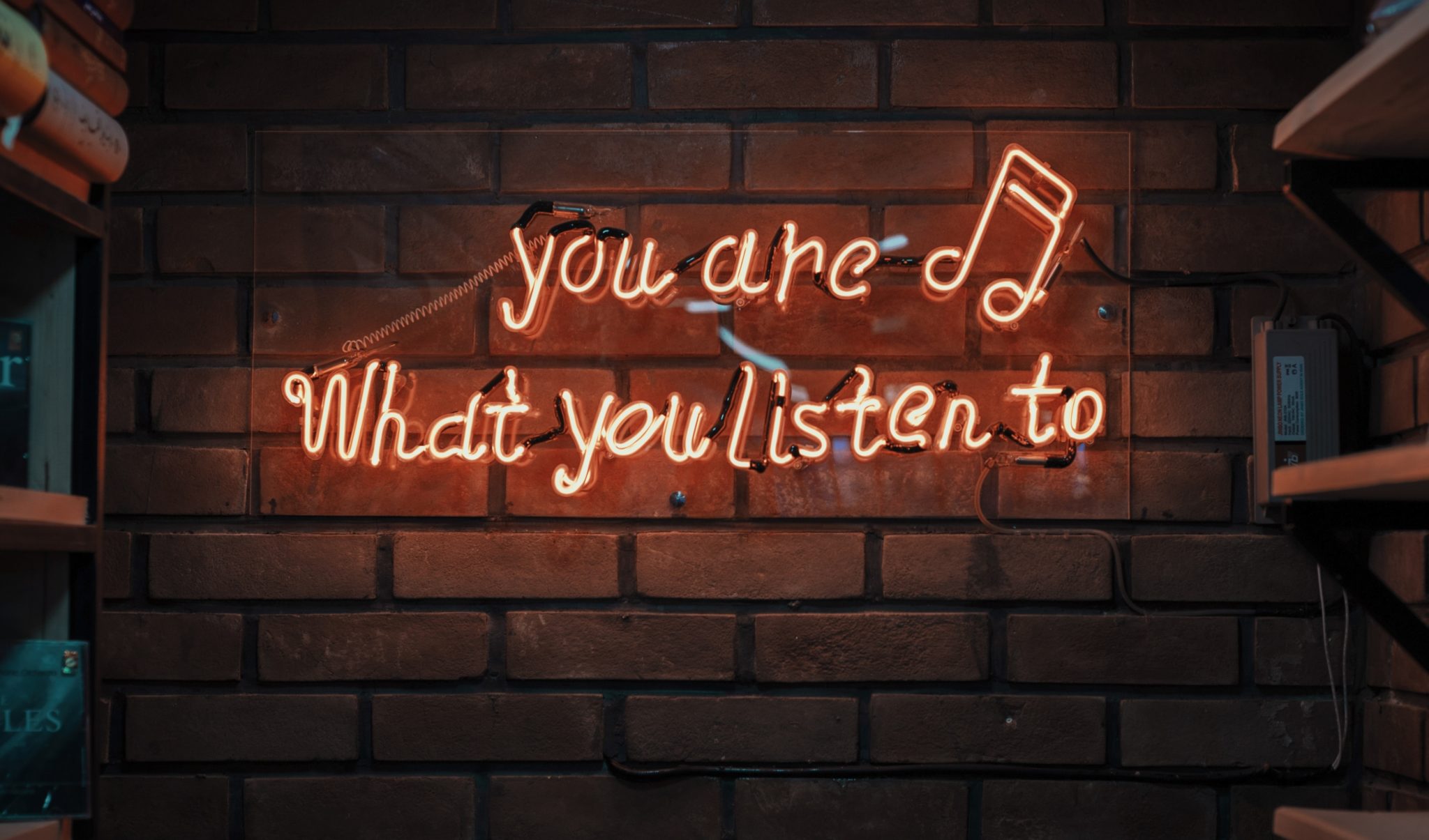 ceglana ściana, a na niej neon z napisem "you are what you listen to"