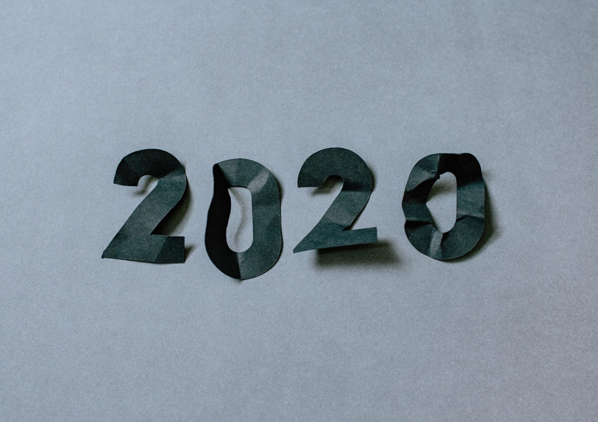 na szarym tle leżą wycięte z czarnego papieru, pogniecione cyfry układające się w numer roku 2020